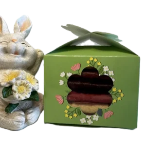 Grüne Oster-Geschenkbox mit Blumen-Stanzung und Pastila-Rollen neben einer weißen Osterhasen-Figur.