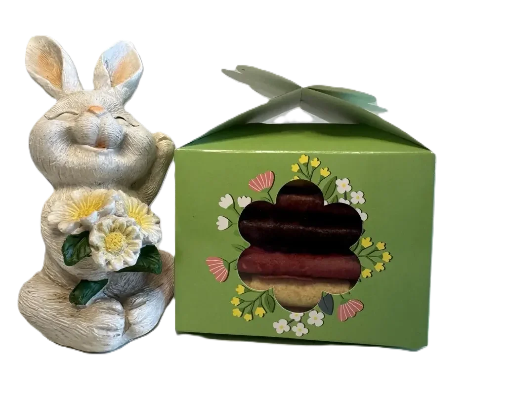 Grüne Oster-Geschenkbox mit Blumen-Stanzung und Pastila-Rollen neben einer weißen Osterhasen-Figur.