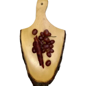 Eine Rolle dunkelrotes Fruchtleder und frische rote Weintrauben auf einem Holzbrett vor weißem Hintergrund.