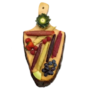 Buntes Fruchtleder in Rollen auf einem Holzbrett mit frischen Erdbeeren, Himbeeren, Weintrauben und Ananas-Deko.