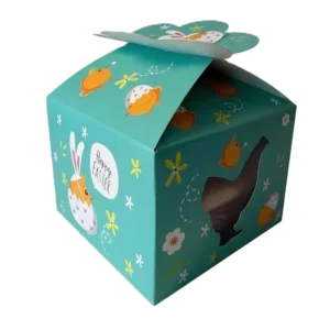 Lilia Oster-Geschenkbox mit gelben Küken, Blumen und 'Happy Easter'-Schriftzug, dazu ein seitliches Sichtfenster.