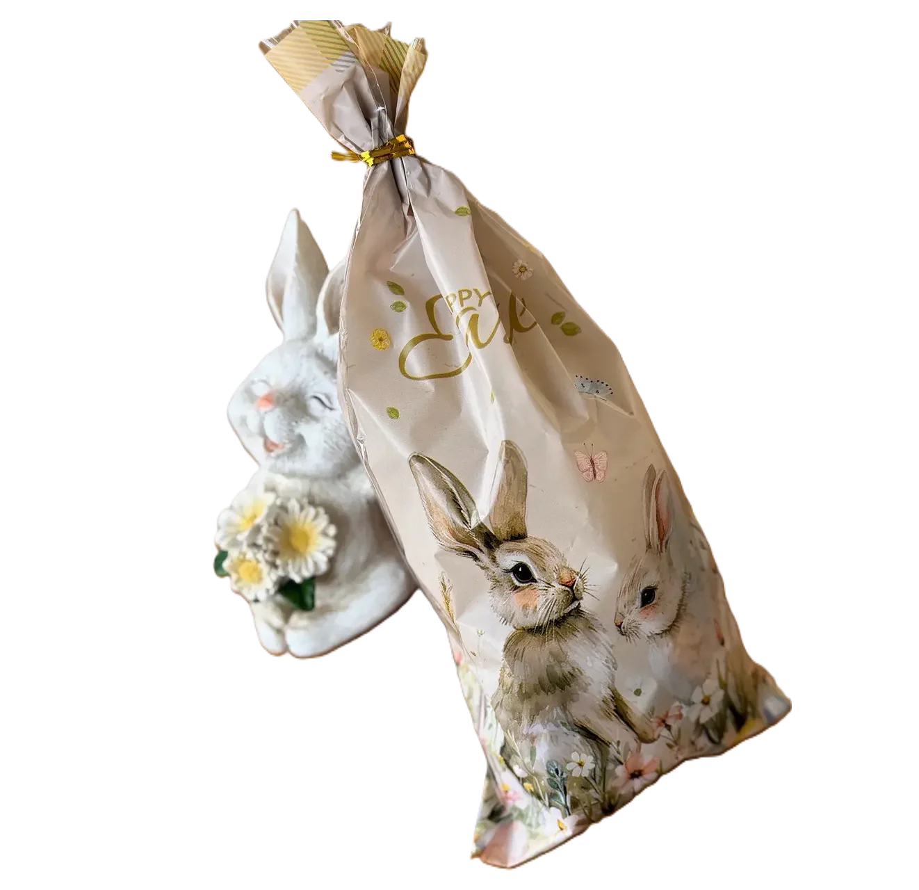 Eine österliche Geschenktüte mit Hasen-Print neben einer weißen Deko-Hasenfigur auf weißem Hintergrund.