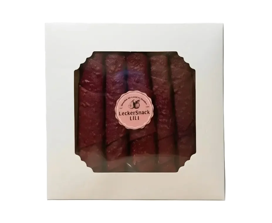 Weiße Geschenkbox mit Sichtfenster, gefüllt mit zahlreichen dunkelroten Himbeer-Fruchtleder-Rollen und Siegel.